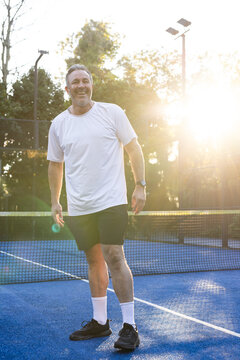 Middle-aged man wearing sportswear standing on blue court near net, watch and lens flare glinting