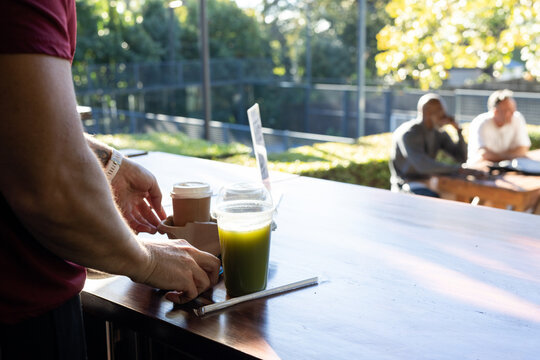 Three men, mature male handling cup carrier at outdoor cafe counter wearing wristwatch, copy space