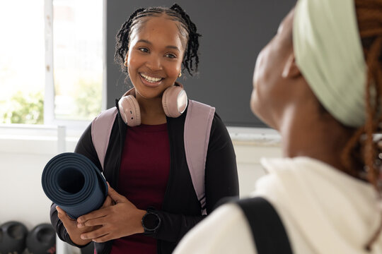 African American adult women smiling and talking while holding rolled blue yoga mat, kettlebells