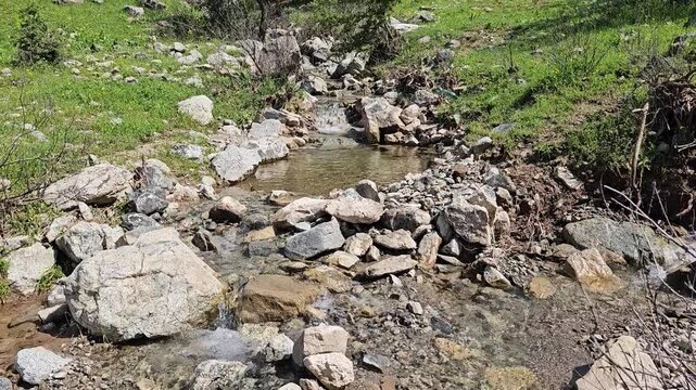 Clear flowing stream winds down a rocky streambed between lush green hillsides, framed by trees under a bright blue spring sky.
📍 Marivan, Kurdistan, Iran 