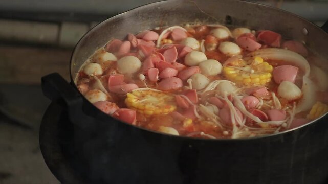 Close-up of a rich mixed hotpot with sausages, fish balls and enoki mushrooms simmering over clay stove