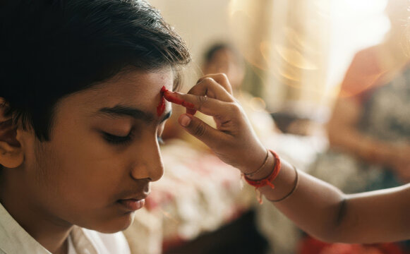 Young Indian boy receiving tilak on forehead during traditional ceremony by sister