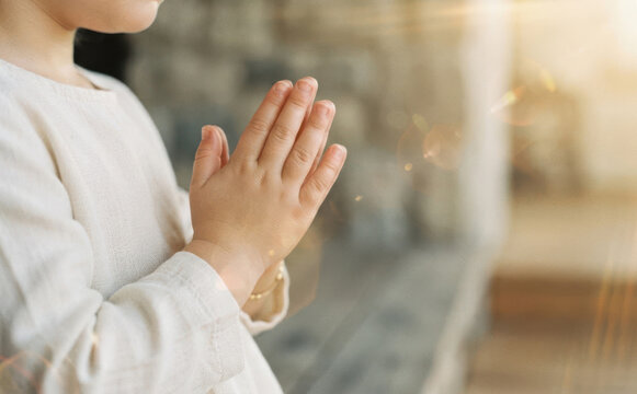 Young child hands clasped together in prayer indoors representing faith spirituality and hope