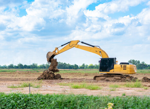 Heavy excavator vehicle scooping and piling dirt on open field land for groundwork and civil engineering construction project.