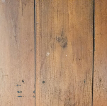 Close-up permukaan panel kayu cokelat dengan serat vertikal, sambungan gelap, sekrup, noda, dan bekas pemakaian yang memberi karakter rustic.
