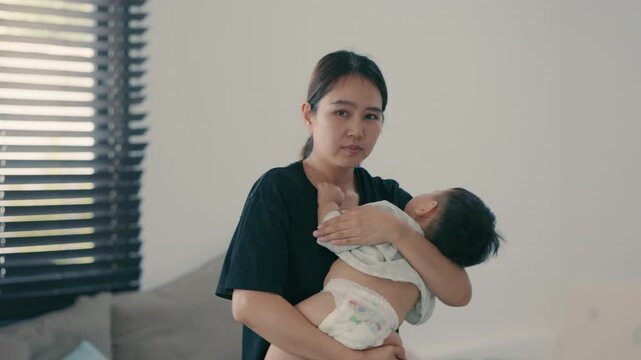 Loving Asian mother holding and comforting her infant baby in arms at home.