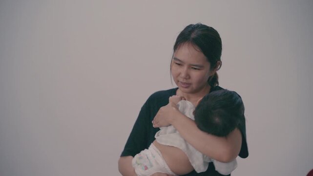Loving Asian mother holding and comforting her infant baby in arms at home.