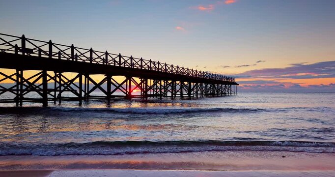 Wooden Pier Bridge on the beach at Sunset Over Calm Ocean Waves on Sandy Beach with Colorful Sky