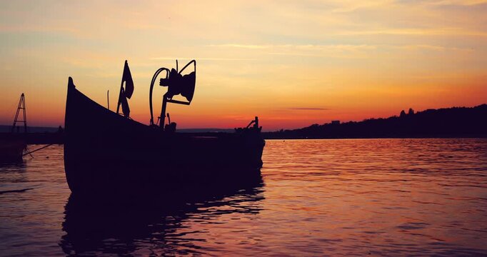 Fishing Boat Silhouette At Sunset Over Calm Water With Orange Sky And Reflective Surface