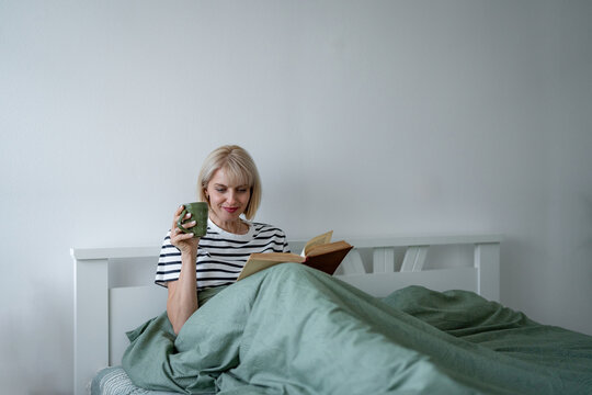Woman reading book and drinking coffee in bed