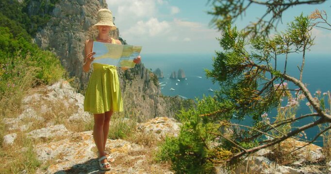 Visitor woman standing on rocky Capri viewpoint admiring Faraglioni sea stacks on summer day