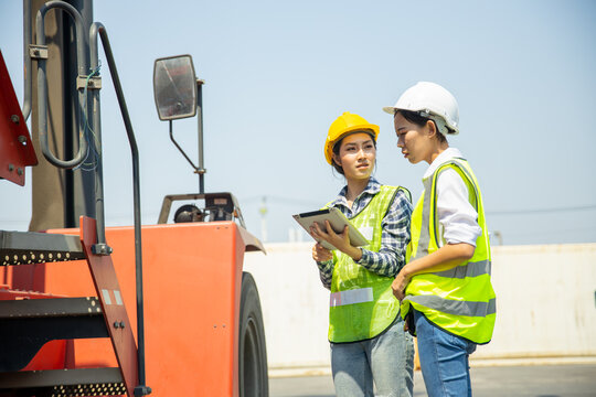 Two female engineers inspecting forklift using tablet at container yard