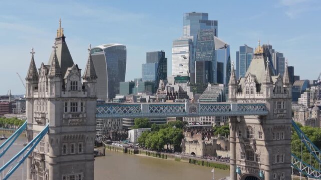 Aerial view of iconic London tower bridge crossing river Thames with modern financial district skyline in background during summer day.