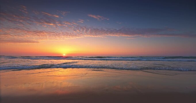 Golden Sunrise Over Calm Ocean Beach Shore With Gentle Waves Splashing on the Reflective Wet Sand and Sea Horizon
