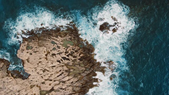 Swells crash around rocky shallows and pool-filled coastline terrain from above