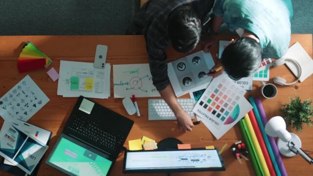 Time lapse of professional designer helping manager choosing color from colored palette. Aerial view of businessman working together and planning together while looking at logo from laptop. Symposium.