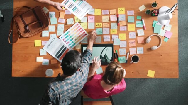 Top view of smart designer holding color palette while project manager looking at design and choosing color for program. Professional businesswoman taking a note while design creative logo. Symposium.