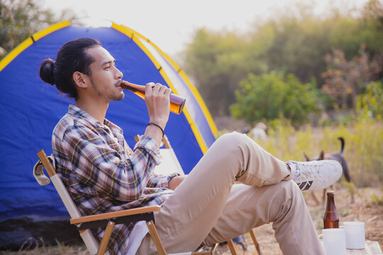 Man relaxing with drink sitting on chair at campsite near tent