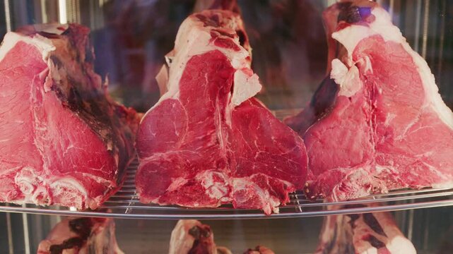 Close up shot of premium dry aged T-bone beef steaks inside glass display fridge at butcher shop.