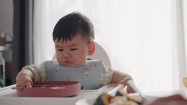 Asian Baby Using Finger to Feed Herself a Food with Baby Led Weaning Concept.Cute Asian baby boy eating finger food in high chair.