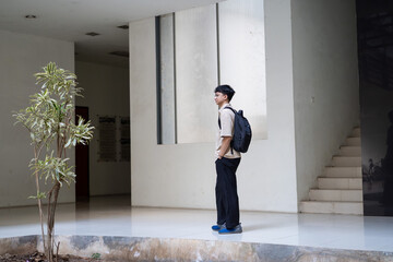 A young man stands in a modern, minimalist interior space with large windows. © Firman Maulana Ihsan