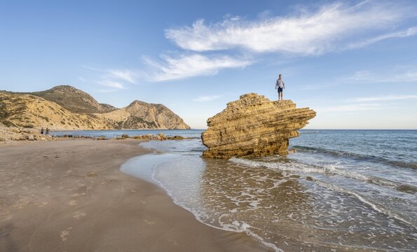 Young man standing on a rock, rocks in the water, sandy beach with rocky cliffs, Paralia Paradisos, Kos, Dodecanese, Greece
