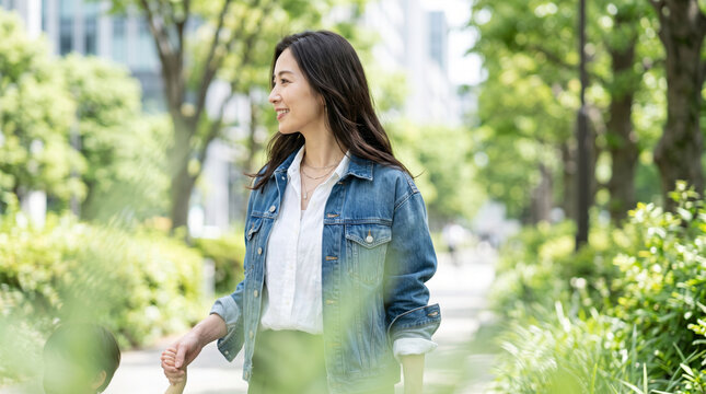 新緑の並木道を子供の手を引いて笑顔で散歩する母親