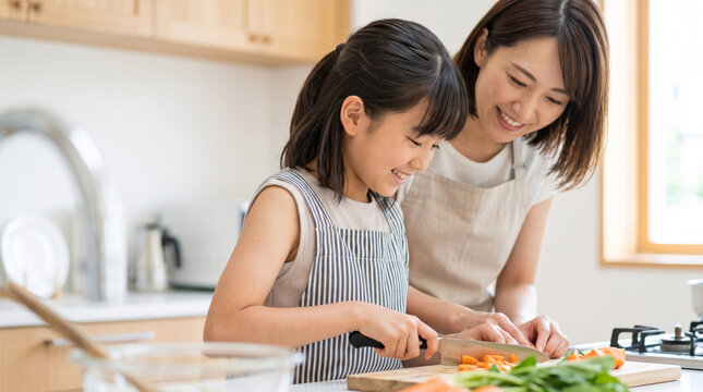 明るいキッチンで母親に見守られながら料理をする女の子