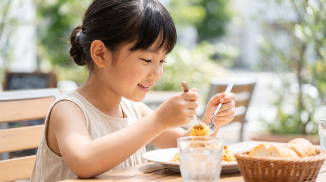 カフェのテラス席で笑顔でパスタを食べる女の子