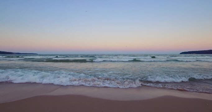 Gentle ocean waves crashing on sandy beach shore at twilight background