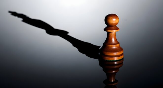 Wooden chess pawn casting a long, powerful shadow on a reflective surface, symbolizing ambition and strategy.