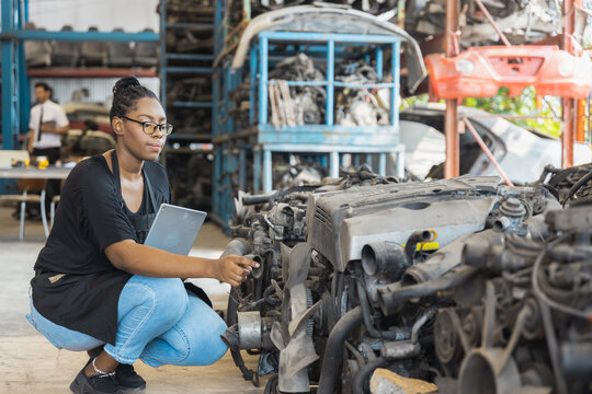 Black female worker with tablet checking car engine inventory in industrial warehouse studio