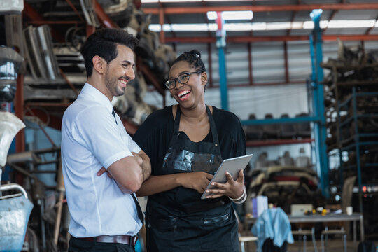 Diverse business partners using tablet to check auto parts in industrial warehouse storage