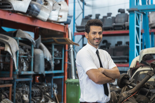 Confident businessman standing with arms crossed in auto parts warehouse and scrap yard