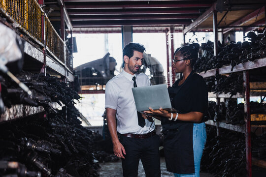Professional Asian doctor and Black woman using tablet in industrial auto parts warehouse