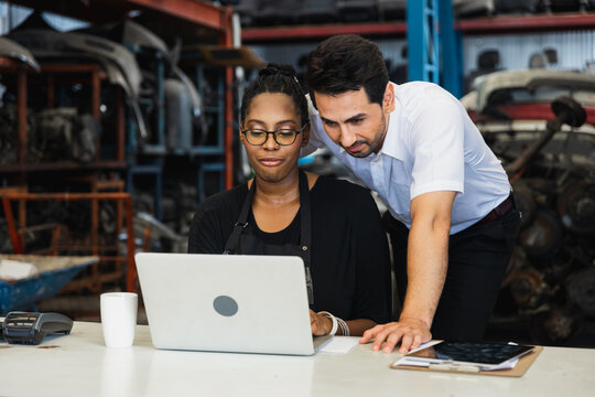 Diverse mechanics collaborating with laptop in automotive repair workshop