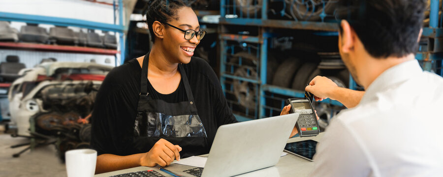Female mechanic processing card payment with customer at auto repair shop counter