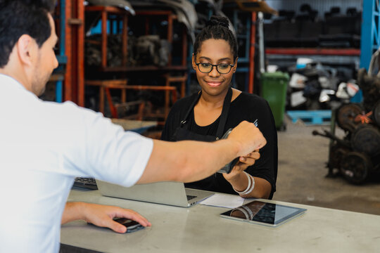 Female mechanic processing card payment with customer at auto repair shop counter