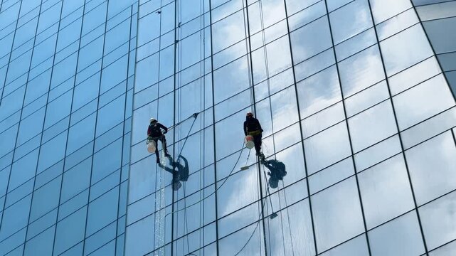 Two Window Cleaners on Blue Glass Skyscraper Curtain Wall