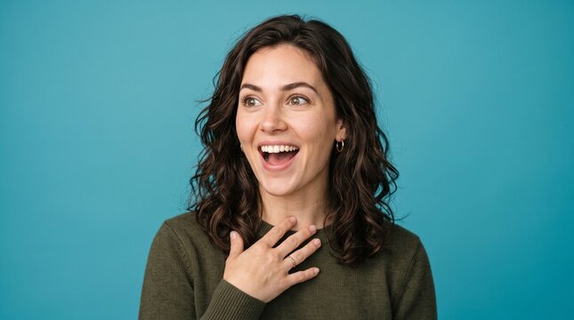 Cheerful young woman with curly brown hair looking away in surprise and excitement against a vibrant blue studio background