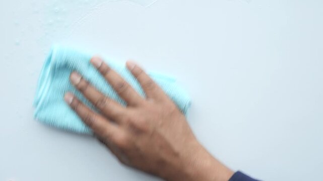 Person cleaning white surface with blue microfiber cloth in motion