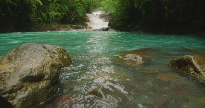 Turquoise river pool in Costa Rica rainforest with small waterfall in vibrant green wild nature