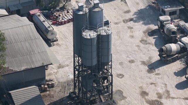 Industrial concrete mixing facility with stationary silos and trucks parked on site during daytime