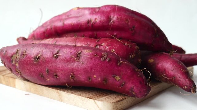 Pile of fresh raw purple sweet potatoes on wooden cutting board with white background