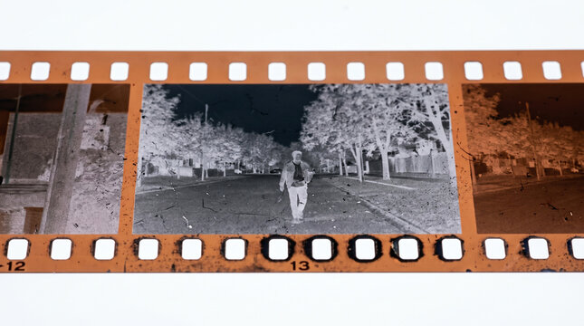 A strip of 35mm photographic film negative showing frames of an outdoor scene with a person walking.