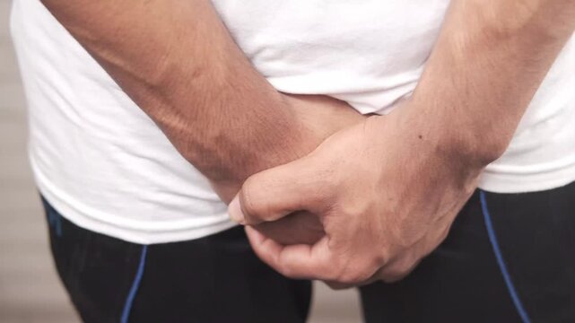 Young man experiencing discomfort in groin area holding his crotch due to pain or medical issues