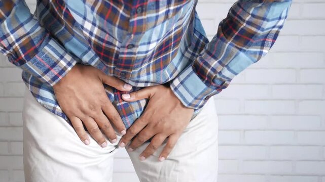 A male wearing casual clothing holding his groin in pain, suffering from an infection or disease, urinary problem footage