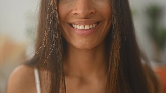 Woman smiling with visible teeth and long hair, bare shoulders and white strap in a studio interior portrait; happiness warmth.