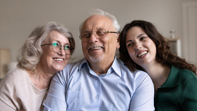 Portrait of happy senior grandparents and young adult granddaughter laughing at home. Loving multigenerational family spend time together, showing connection, harmony in relationships and strong bond