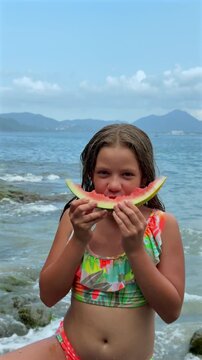 Niña rubia latina comiendo rebanada de fruta sandia fresca en la costa playa del océano pacífico en Manzanillo Colima México toma vertical